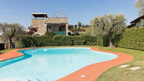 A swimming pool with a curved edge, surrounded by a brick pathway and a grassy area.