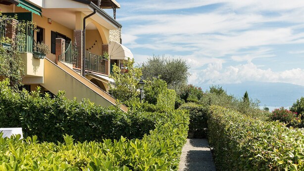 A building with a balcony and a pathway surrounded by greenery.