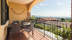 A balcony with a table and chairs, a view of the countryside, and a string of lights on the wall.