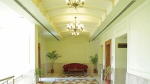 A hallway with a geometric patterned floor, a chandelier, and potted plants. - Hotel Om Tower & Revolving Restaurant  (Jaipur)
