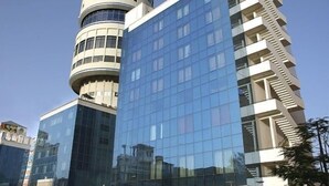 A modern building with a cylindrical tower and a rectangular glass facade. - Hotel Om Tower & Revolving Restaurant  (Jaipur)