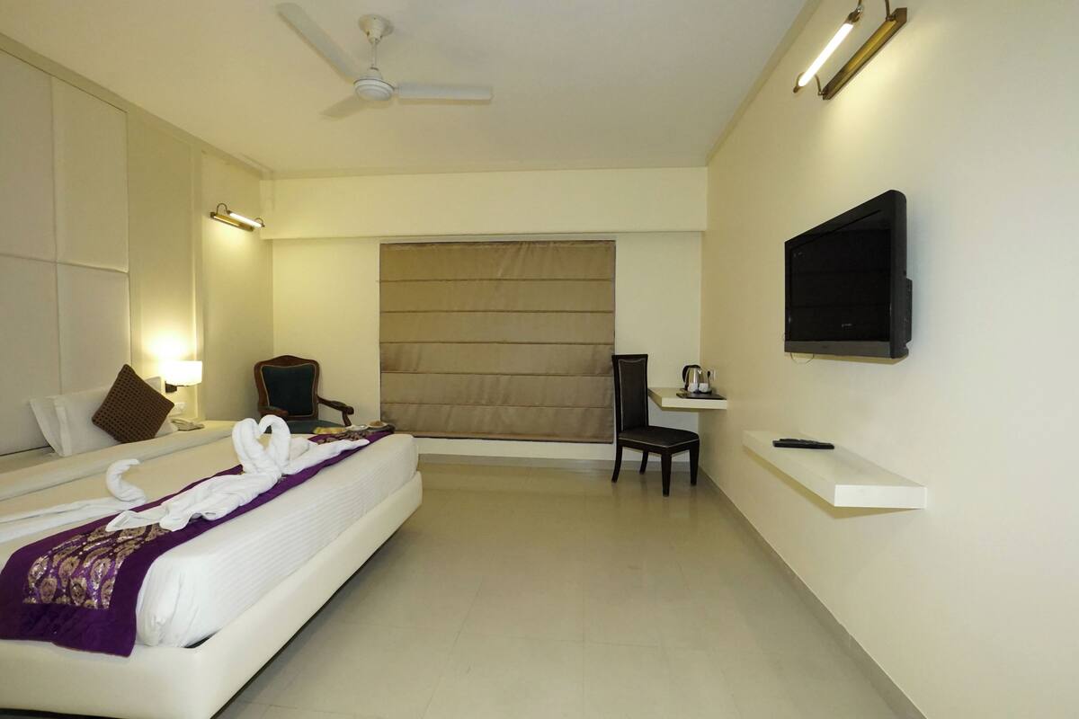 A hotel room with a bed, a chair, a TV, and a desk.