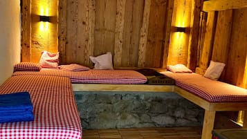 A rustic wooden room with two beds, stone wall, and wooden beams.
