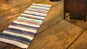 Une pièce avec un plancher en bois, un lit avec une tête de lit blanche, une commode en bois, une chaise et deux tableaux encadrés accrochés au mur.