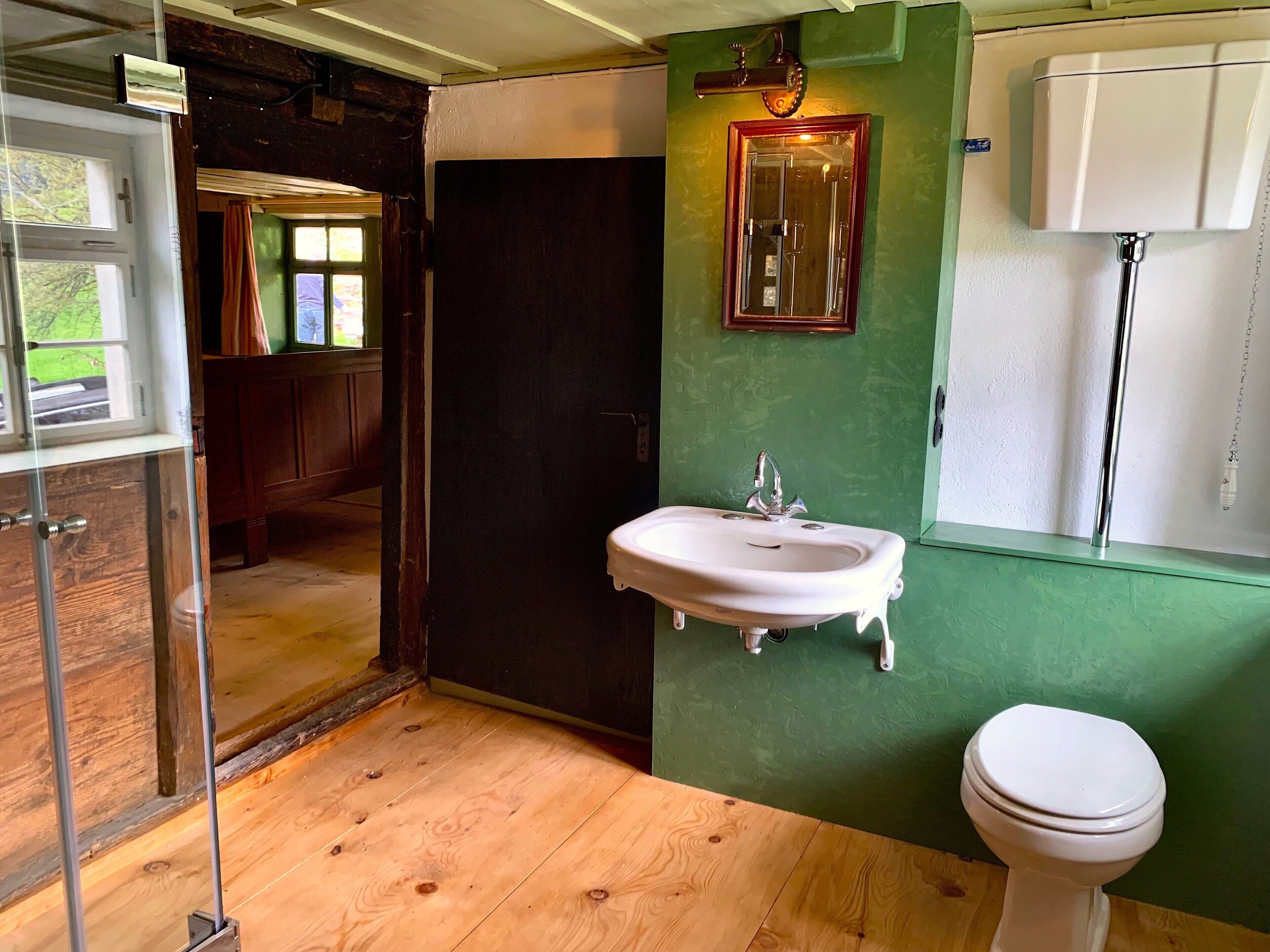 Un bagno con pavimento in legno, un lavandino bianco, uno specchio e un water.