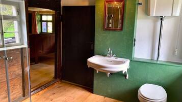 Un baño con piso de madera, un lavamanos blanco, un espejo y un inodoro.