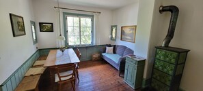 A room with a dining table, chairs, a bench, a window with curtains, and a green cabinet with a pipe.