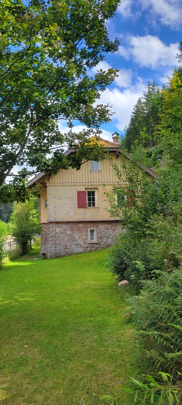 A two-story house with a stone foundation, a red door, and a thatched roof.