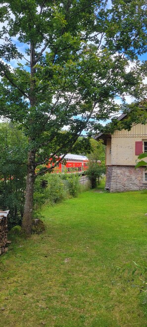 A stone building with a red door, surrounded by a grassy area and trees.