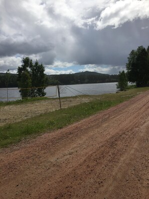 A dirt path leading to a fenced area with a body of water and trees in the background. - Villa Tina (Hammarstrand)