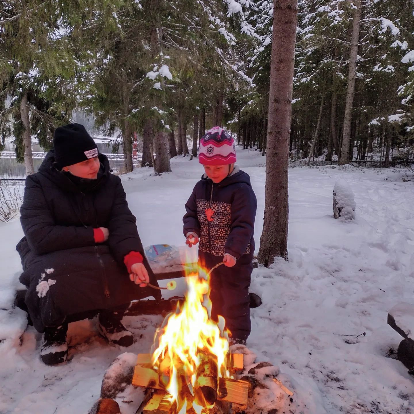 Two people sitting by a campfire in a snowy forest.