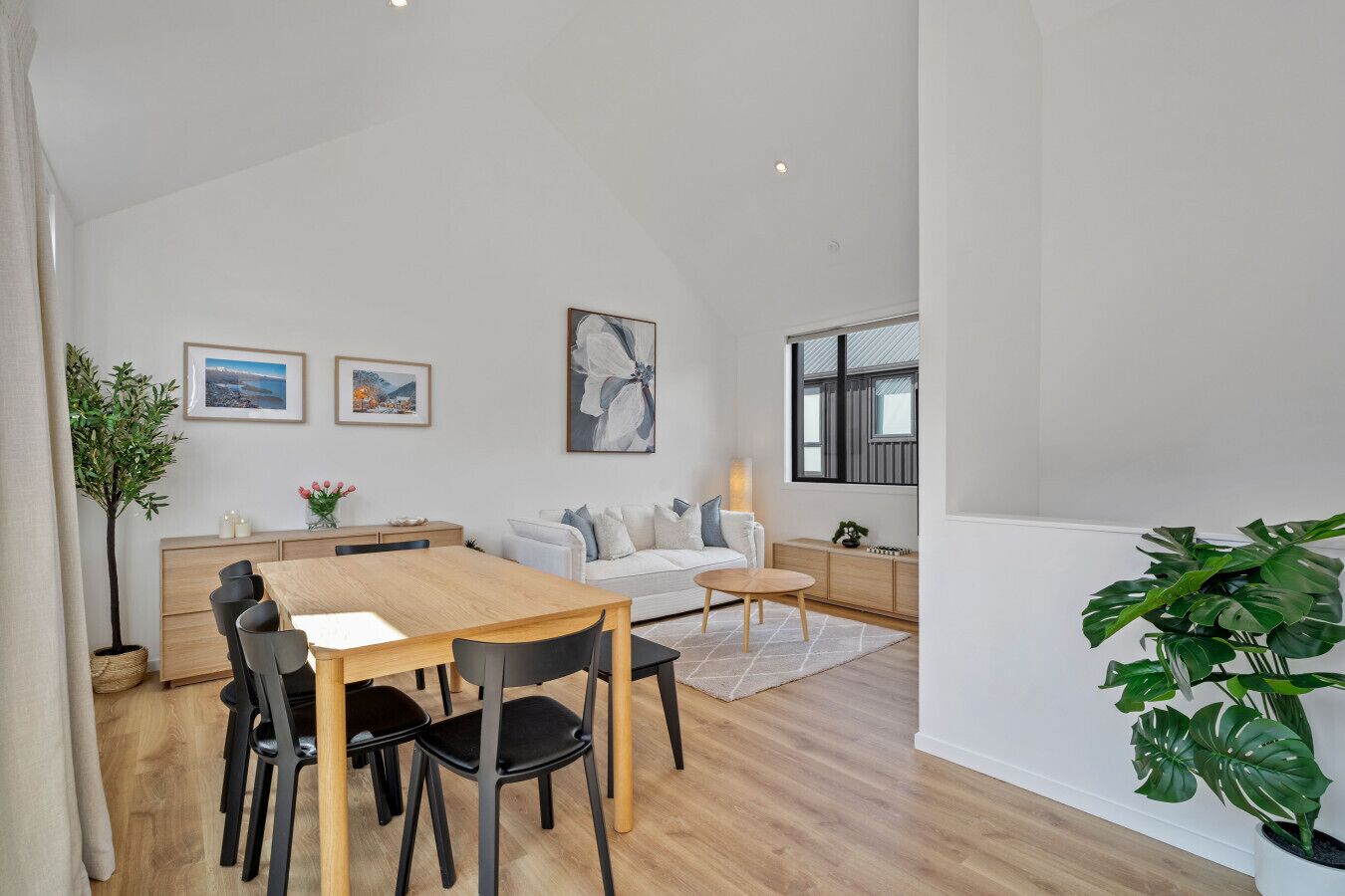 A modern living room with a dining area, a sofa, a coffee table, and a large window.