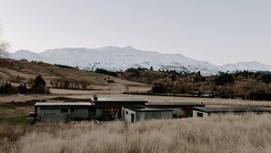 Een modern gebouw met een plat dak en grote ramen, omringd door een grasveld en een met sneeuw bedekte bergketen op de achtergrond.