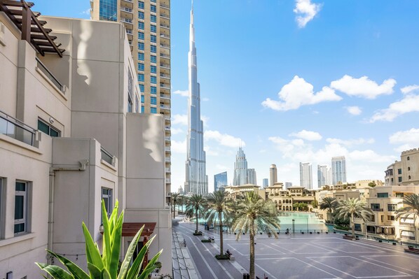 A modern urban scene with a prominent skyscraper, palm trees, and a spacious plaza.