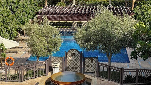 A pool area with a hot tub, surrounded by a fence and trees. -  Durrani Homes - Azure 2BR with Burj Khalifa and Fountain View (Dubai)