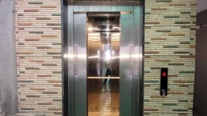 An elevator with a metallic finish, a control panel on the right, and a patterned wall on either side. - HOTEL ARADHANA (Veraval)