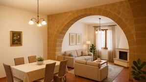 A dining area with a table and chairs, a sofa, a fireplace, and an arched stone wall.