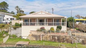A two-story building with a balcony, a small deck, and a stone wall in the foreground. - Tide view - A waterfront retreat with a BBQ, Kayak (Toukley)
