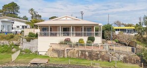 A two-story building with a balcony, a small deck, and a stone wall in the foreground. - Tide view - A waterfront retreat with a BBQ, Kayak (Toukley)