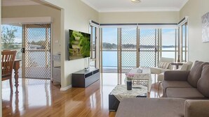 A living room with a television, a sofa, a coffee table, and a view of the water. - Tide view - A waterfront retreat with a BBQ, Kayak (Toukley)