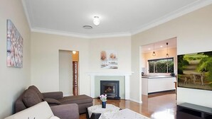 A living room with a fireplace, a sofa, a TV, and a kitchen area. - Tide view - A waterfront retreat with a BBQ, Kayak (Toukley)
