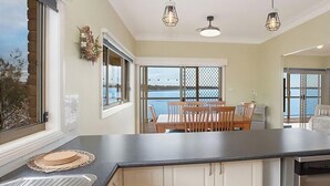 A kitchen with a large island, a dining area with a table and chairs, and a view of the sea through large windows. - Tide view - A waterfront retreat with a BBQ, Kayak (Toukley)