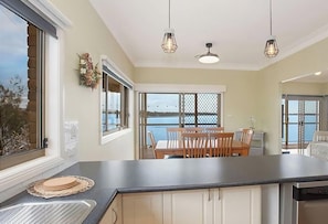A kitchen with a large island, a dining area with a table and chairs, and a view of the sea through large windows. - Tide view - A waterfront retreat with a BBQ, Kayak (Toukley)