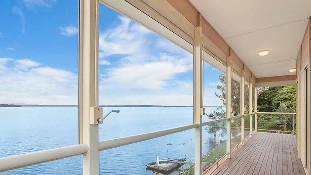 A view from a balcony with large windows overlooking a calm body of water and distant land. - Tide view - A waterfront retreat with a BBQ, Kayak (Toukley)