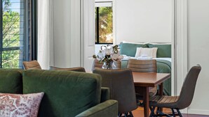 A modern room with a green sofa, a wooden table, and a bed with a green headboard. There is a window with a view of greenery outside. - Havenwood Chalet 2 Bedrooms (Ravensbourne)