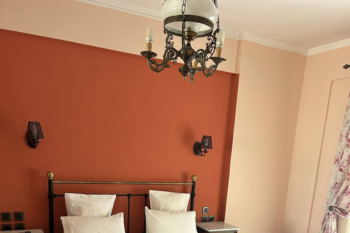 A neatly made bed with white linens and a striped blanket, a bedside table with a lamp, and a chandelier above.