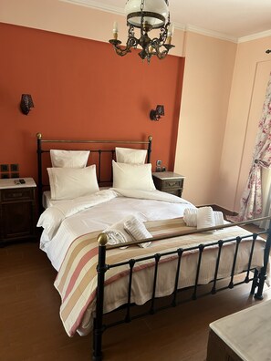 Una cama bien hecha con sábanas blancas y una manta a rayas, una mesita de noche con una lámpara, y un candelabro arriba.