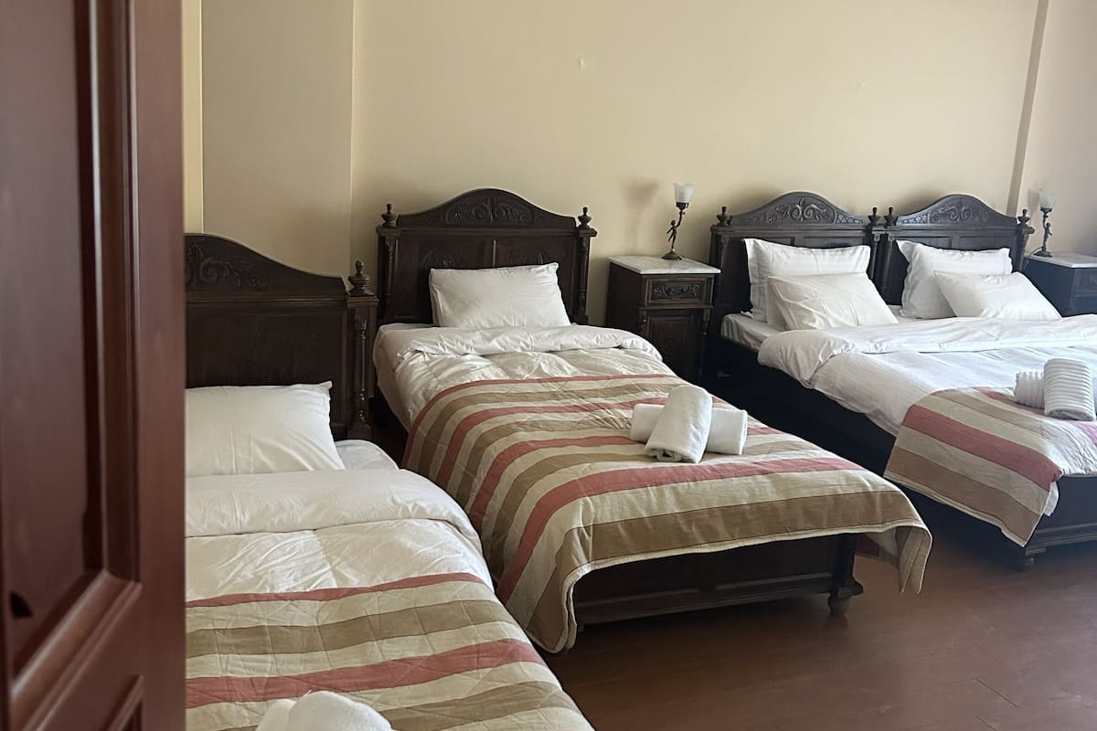 A hotel room with three beds, each with a wooden headboard and white linens.