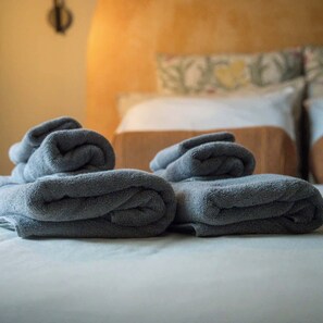 Un lit bien fait, avec des serviettes grises pliées et une lampe en arrière-plan.
