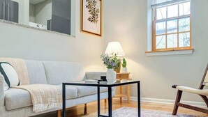 A living room with a sofa, a coffee table, a lamp, a chair, a window, and a framed botanical print on the wall. - Cozy 1BD In The Heart Of Rittenhouse Square (Philadelphia)