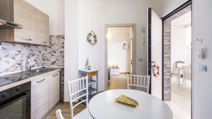 Una cocina moderna con horno empotrado, un lavamanos y una zona de comedor con mesa y sillas blancas.