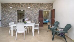 Un patio con pared de piedra, muebles de mimbre blanco y vista a un dormitorio.