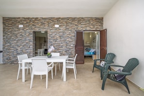 Un'area patio con un muro in pietra, mobili in vimini bianco e vista su una camera da letto.
