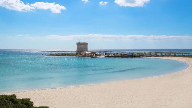 Una playa con agua turquesa cristalina, una orilla de arena y una pequeña estructura tipo torre.