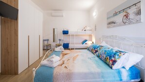 Un dormitorio con una cama litera, un televisor de pantalla plana, un cuadro y una colcha con motivos playeros.