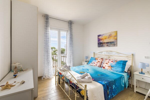 Un dormitorio con cama, mesita de noche, escritorio y ventana con cortinas.