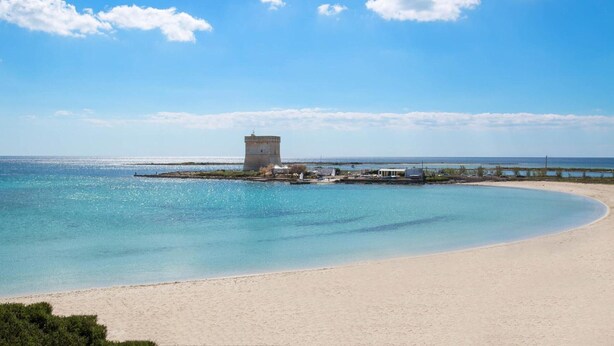 Una spiaggia con una torre, acque cristalline e una riva sabbiosa.
