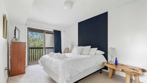 A bedroom with a bed, a wooden bench, a desk, and a view of the outdoors.