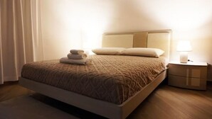 Un lit bien fait, recouvert d’une couvre-lit à motifs, une table de chevet avec une lampe et une petite table de nuit avec un tiroir.
