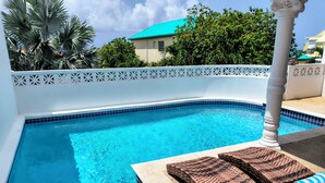 Una piscina con borde de azulejos blancos, rodeada por una valla blanca con adornos recortados.