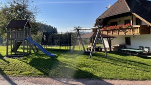 Un terrain de jeux avec un toboggan et des balançoires, une cabane en bois et une maison avec un balcon.