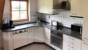 Une cuisine avec des meubles blancs, un four en acier inoxydable, un four à micro-ondes et une fenêtre donnant sur un paysage verdoyant.