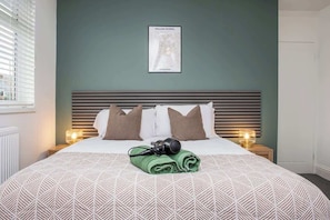A hotel room with a bed, pillows, a framed picture on the wall, and a camera on the bed.