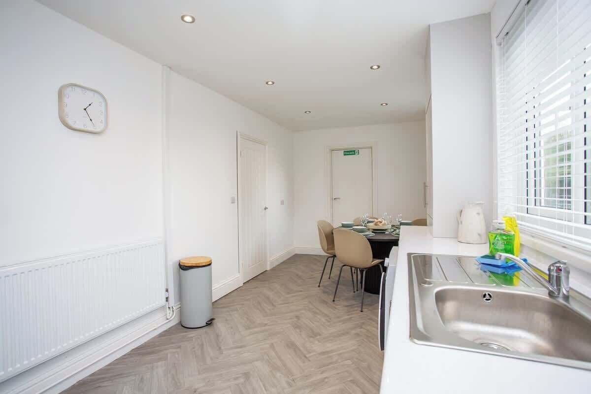 A modern kitchen with a sink, a clock, and a dining area with chairs and a table.