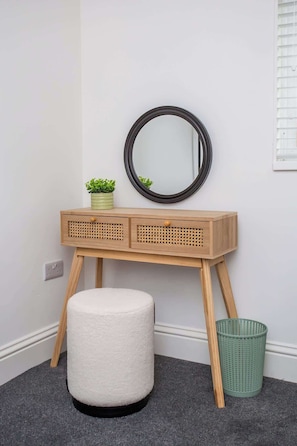 A small, wooden vanity with a round mirror, a small potted plant, and a green basket.