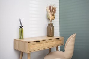 A wooden desk with a vase and reed diffuser, a chair, and a wall with a vertical stripe pattern.